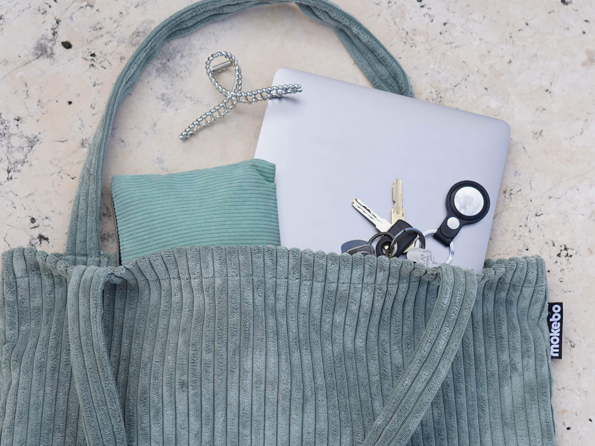 Cordtasche Tote Bag in salbei auf Steinboden, Laptop Schlüssel und Haarklammer schauen heraus 