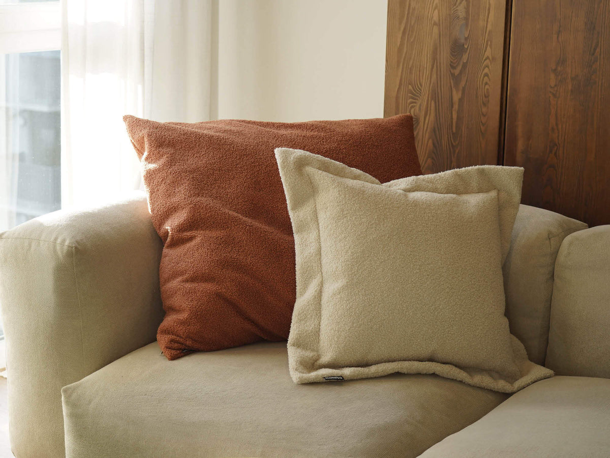 XXL Bouclé Kissen 'Hug' in Terracotta mit Sofakissen Bouclé 'Laze' in beige auf einem Sofa. Kissen sind aneinander gelehnt 