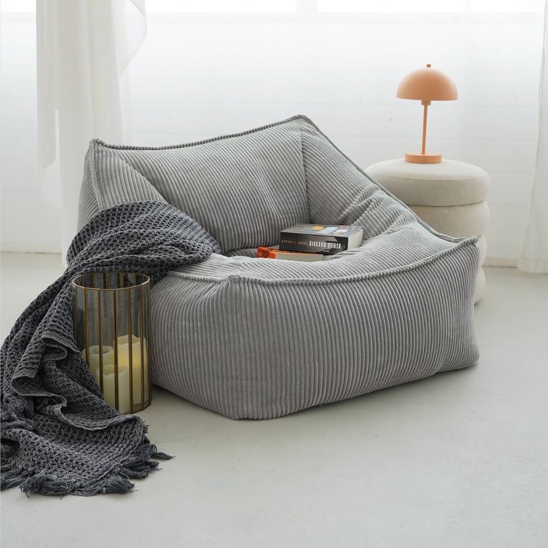 Sitzsack Sitzliege Bean Bag in Cord hellgrau 'Der Lümmel' im Wohnzimmer mit einer Decke, zwei Bücher liegen auf dem Sitzsack. 
